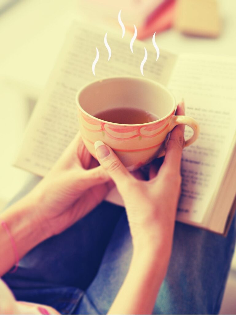 Eine dampfende Tasse Tee und ein Buch liegen auf Beckys Beinen – ein Moment echter Ruhe ohne Meditation